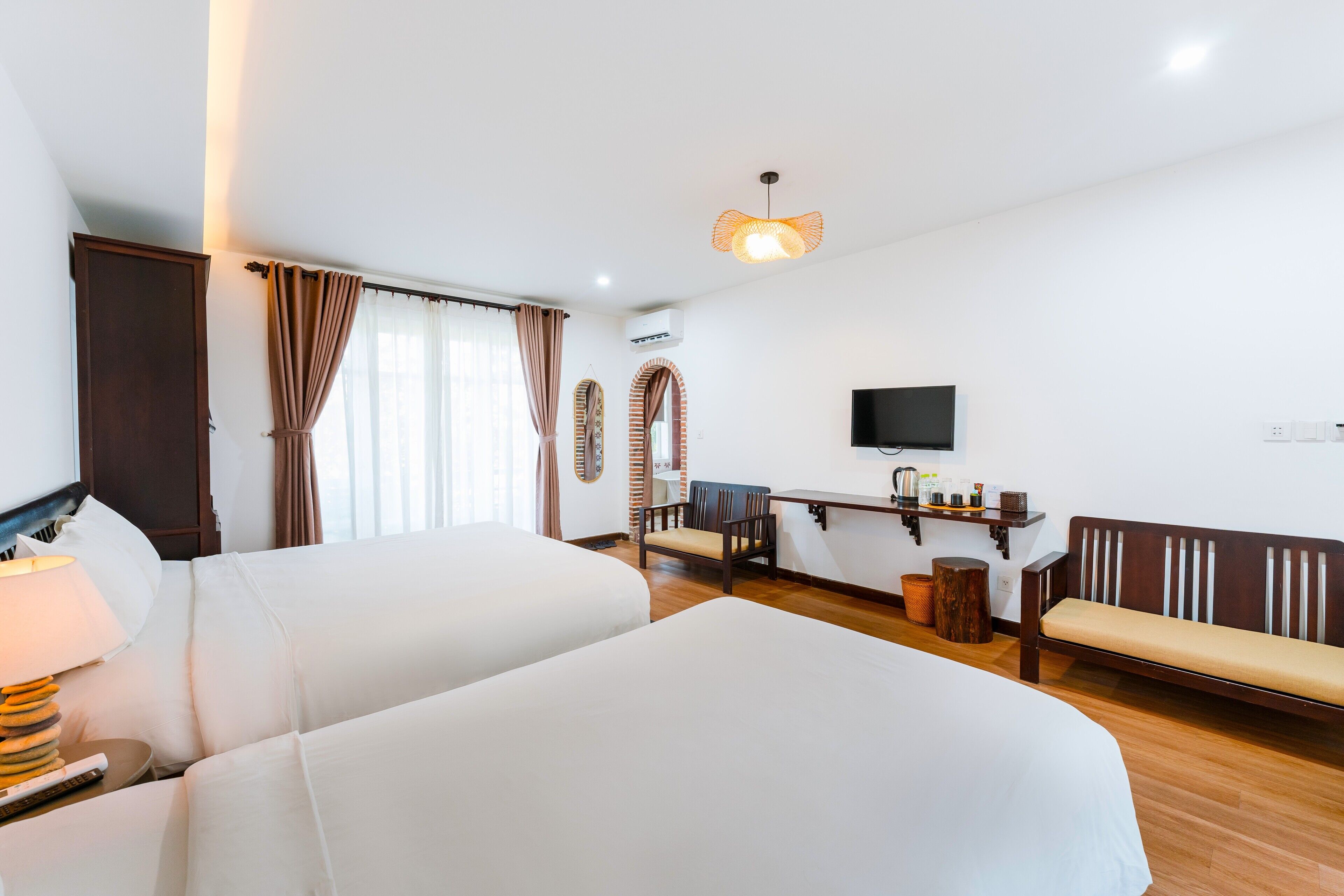 Habitación de hotel con dos camas, un escritorio con silla, un televisor y un banco.