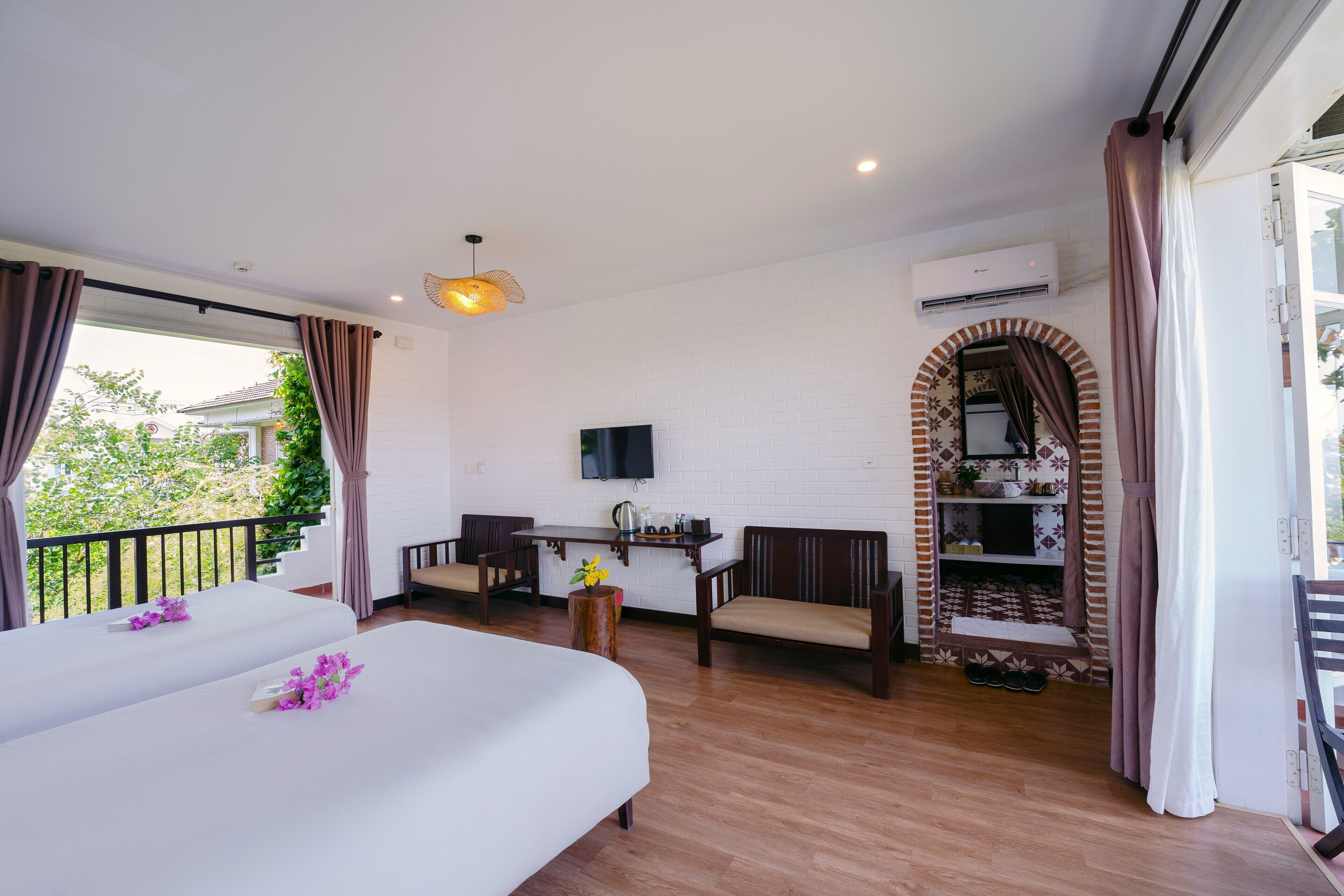 A hotel room with two beds, a dining table, a TV, and an air conditioning unit.
