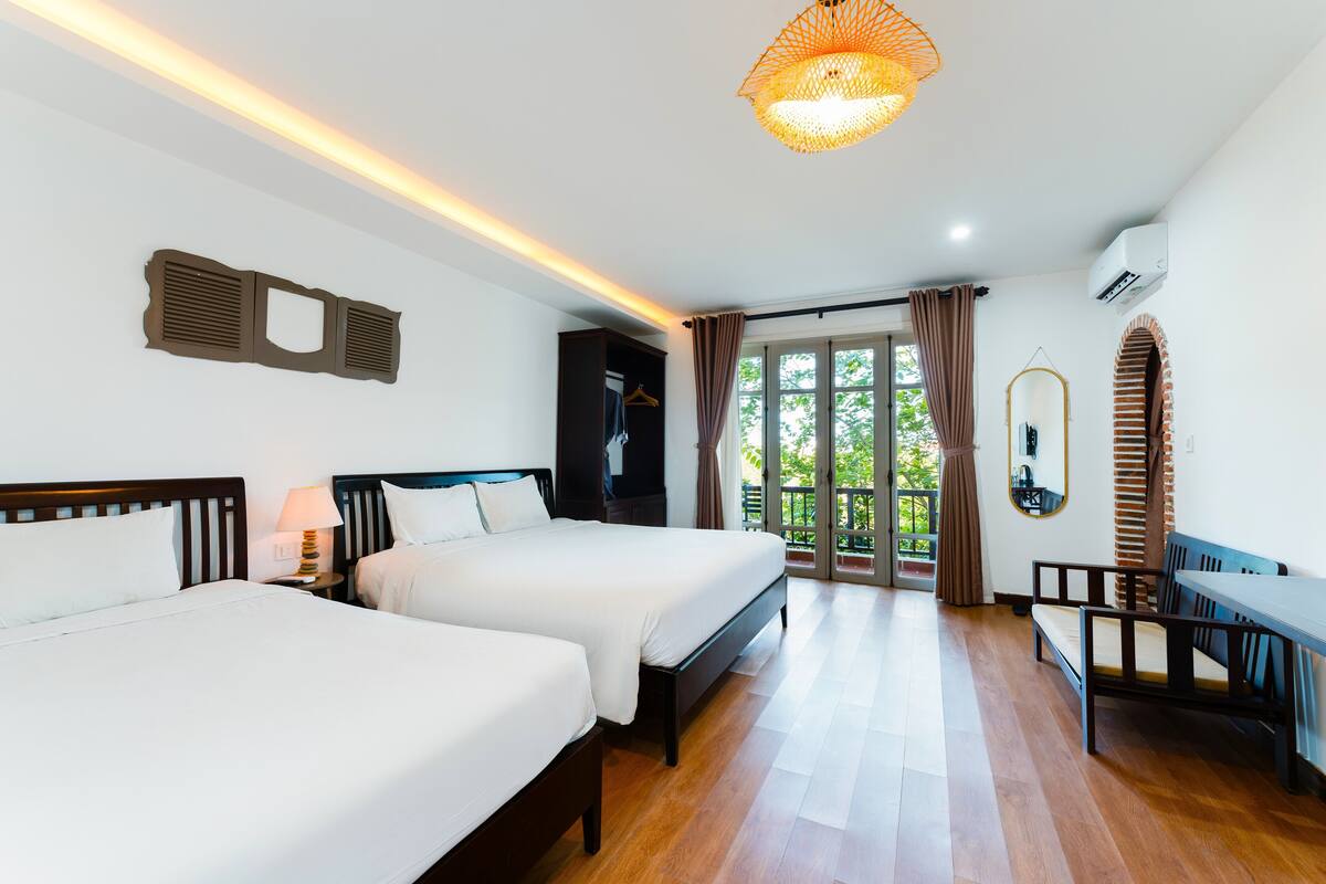 A hotel room with two beds, a desk, and a balcony with curtains.