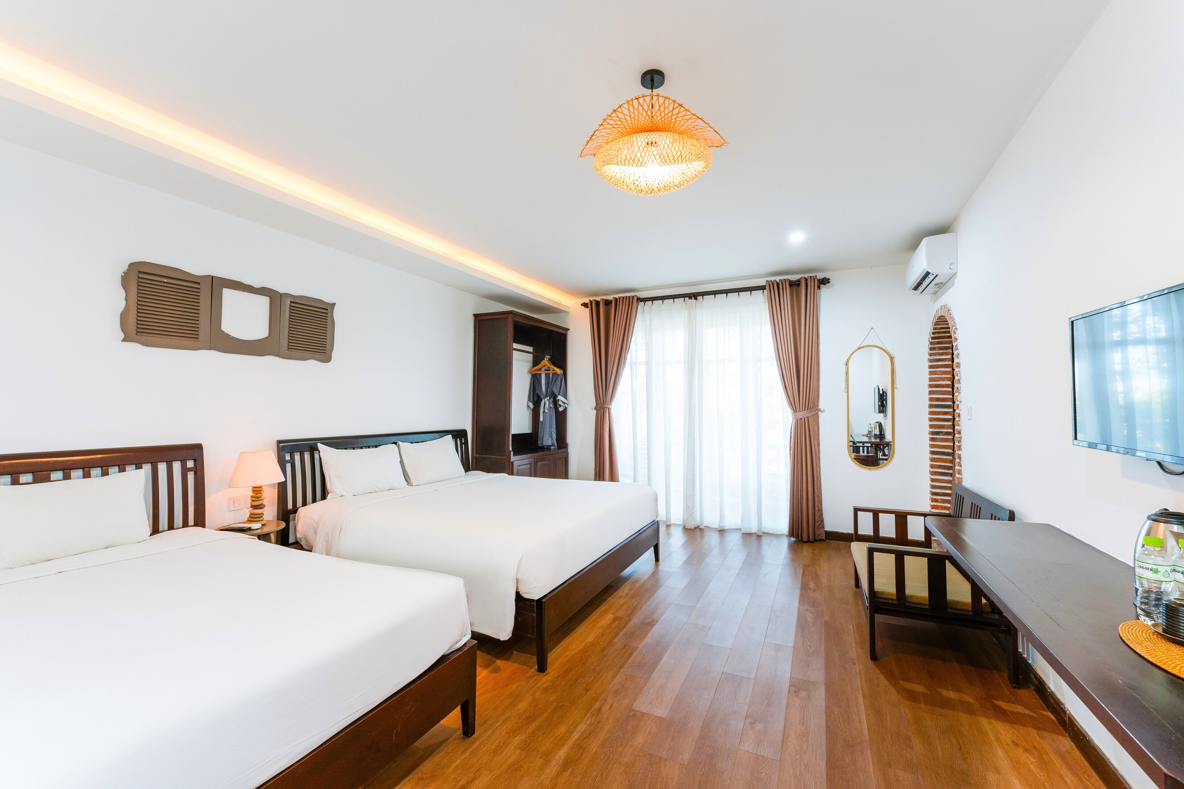 A hotel room with two beds, a desk, a TV, and a hanging light fixture.