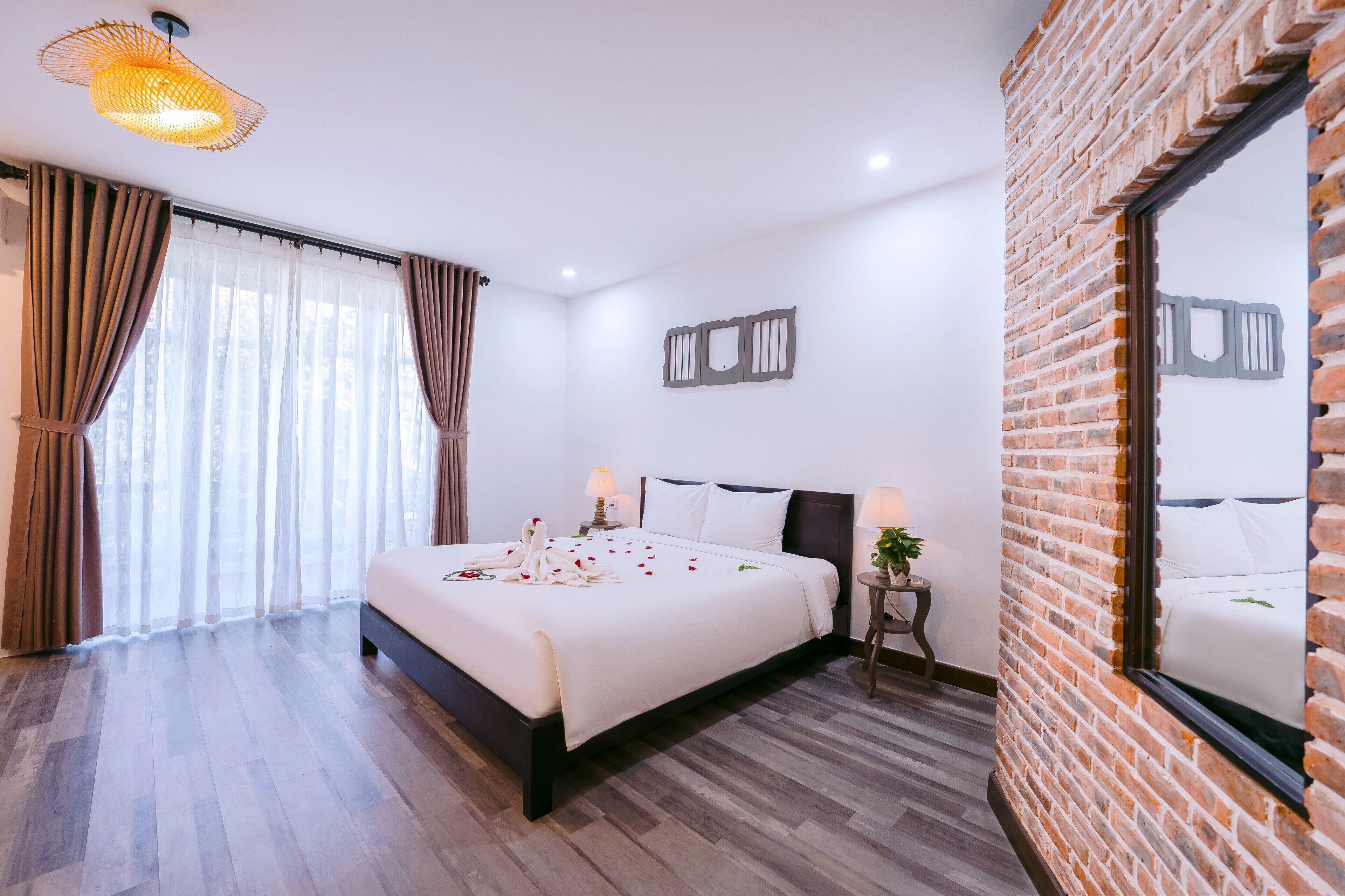 A hotel room with a large bed, a brick accent wall, and a large window with curtains.