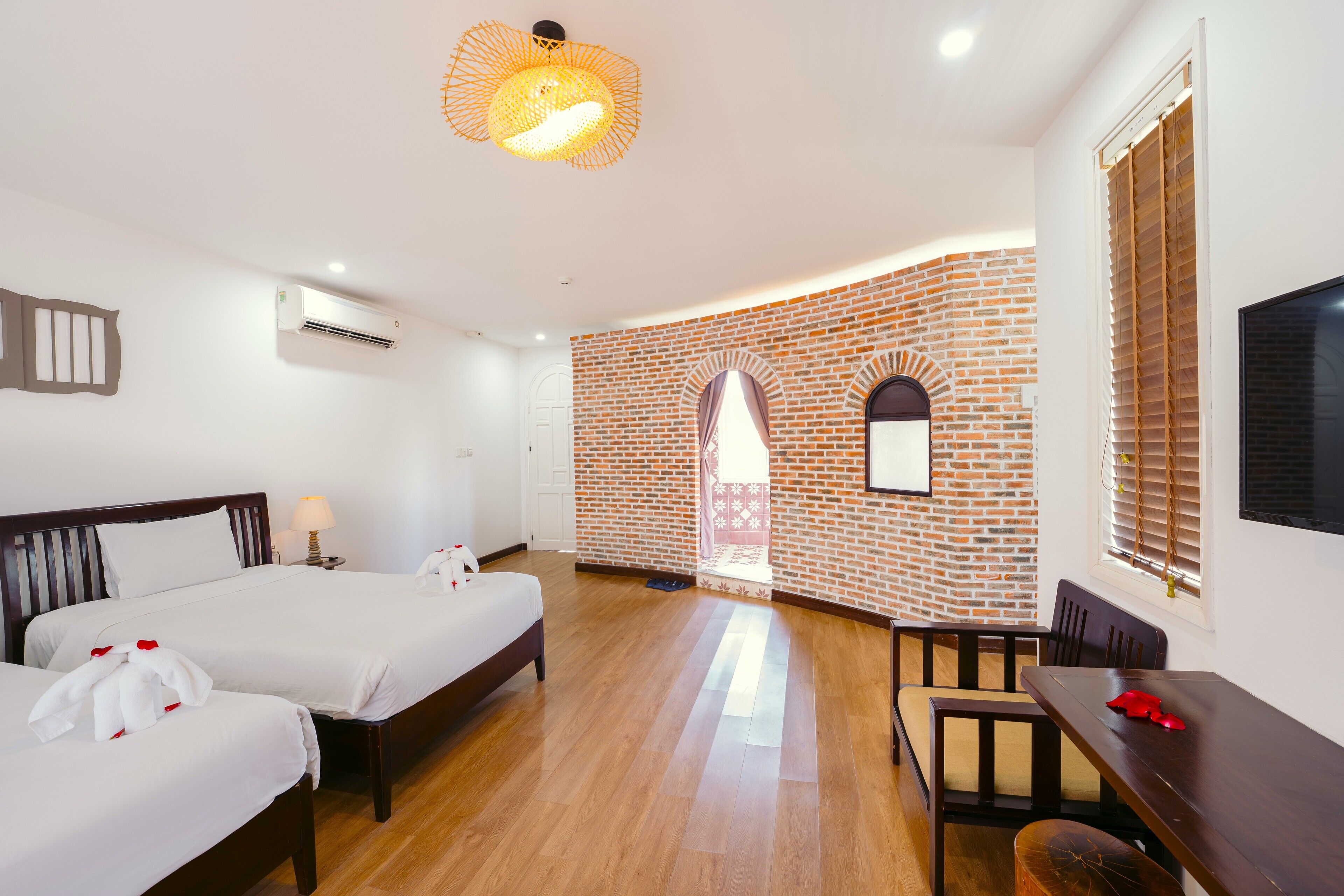 A hotel room with two beds, a dining table, a TV, and a brick wall.