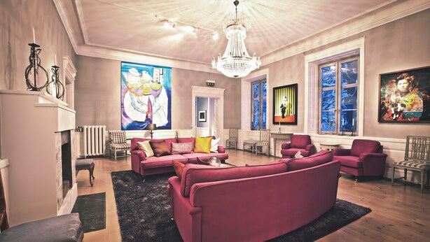 A spacious living room with a large pink sofa set, a chandelier, and artwork on the walls. - Ulvhälls Herrgård (Strängnäs)
