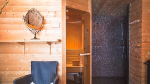 A wooden cabin interior with a wooden chair, a mirror, and a shower area with tiled walls. - Ulvhälls Herrgård (Strängnäs)