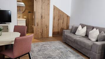 A modern living room with a grey sofa, a dining area with a table and chairs, and a large wooden wardrobe.