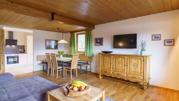 A modern living room with a wooden ceiling, a sofa, a dining table with chairs, a TV, and a wooden cabinet.