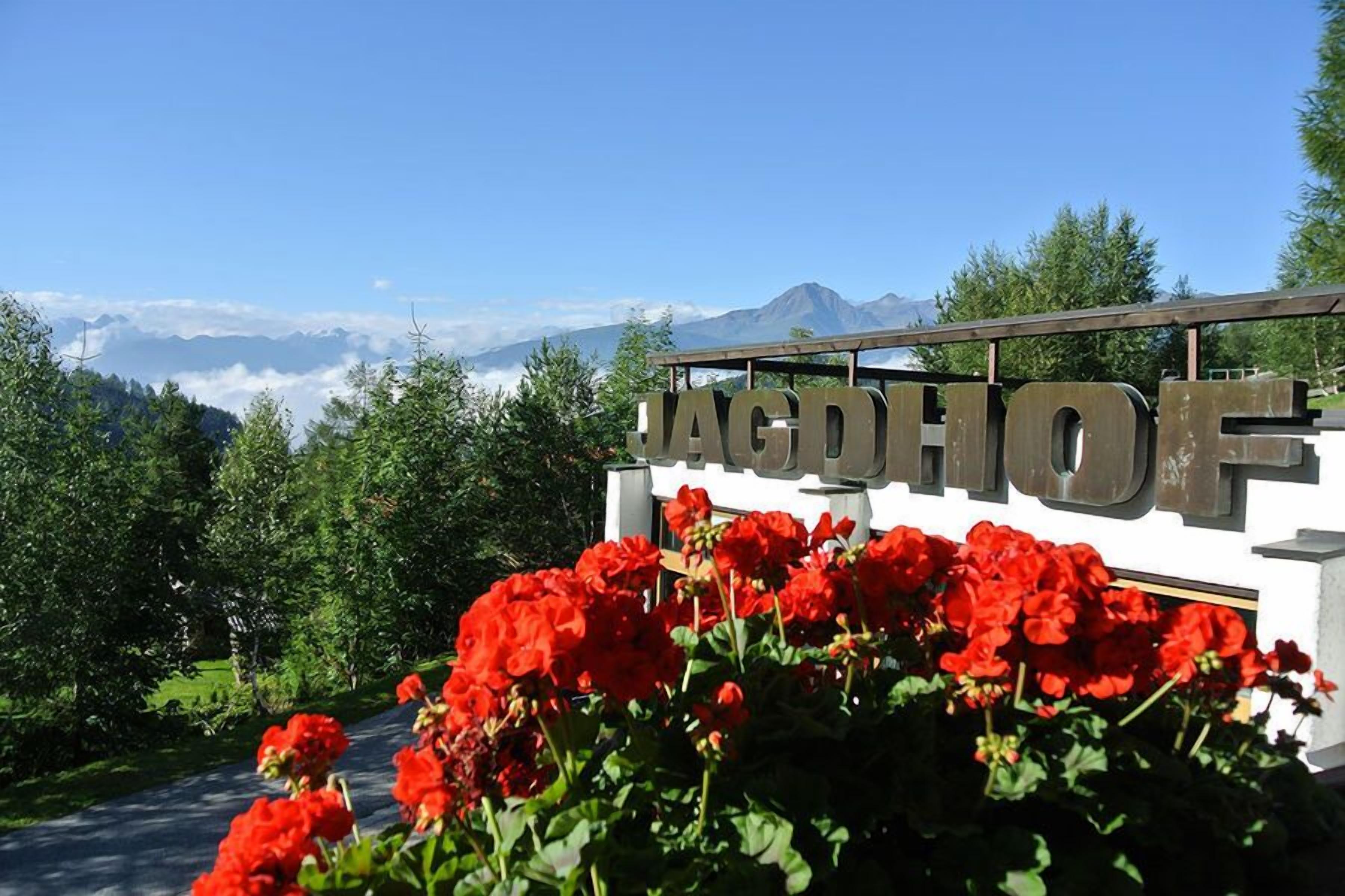 A sign with the name "JAGDFORF" surrounded by red flowers and a mountainous backdrop.