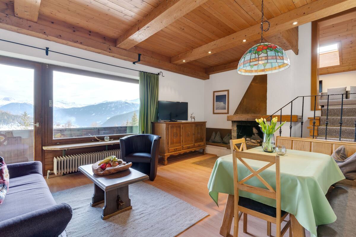A cozy living room with a fireplace, a dining area, and a view of mountains.