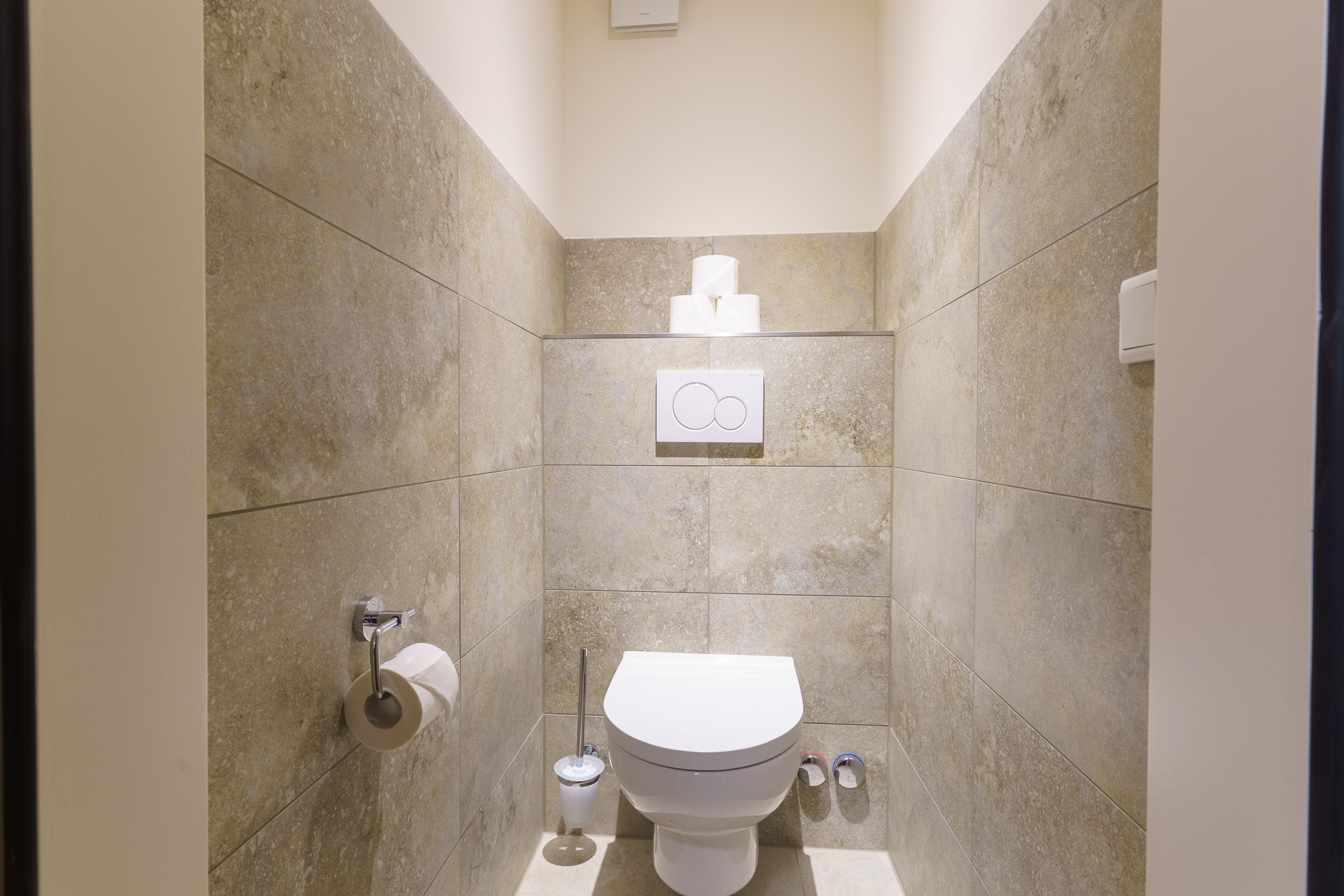 Een moderne badkamer met toilet, handdroger en papieren handdoekdispenser.