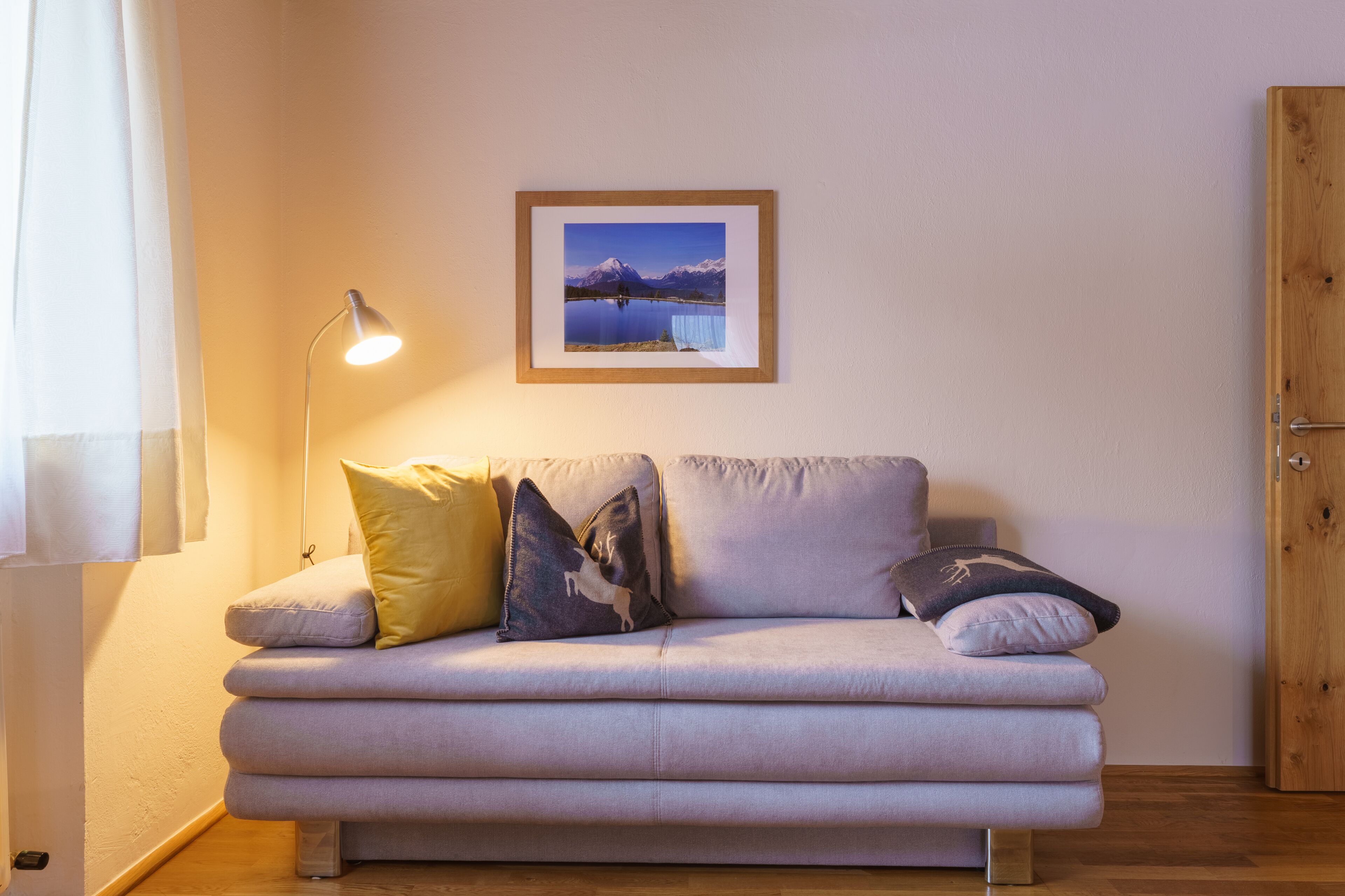 A living room with a sofa, a framed picture on the wall, a floor lamp, and a wooden door.