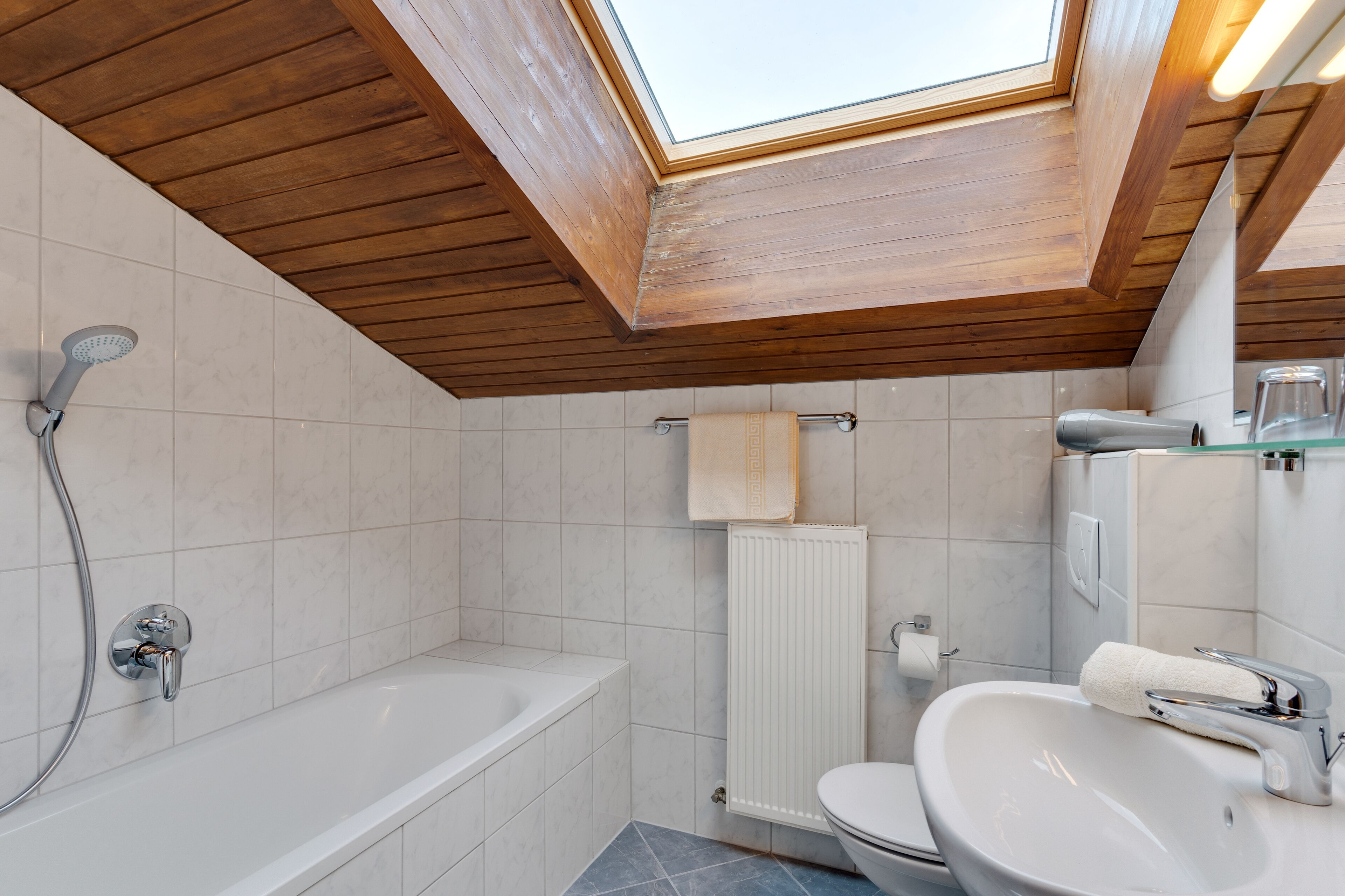 A modern bathroom with a skylight, a bathtub, a sink, and a toilet.