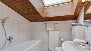 A modern bathroom with a skylight, a bathtub, a sink, and a toilet.