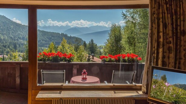 A balcony with a view of mountains, a table with chairs, and a Sony TV. - Apartmenthaus Jagdhof (Reith bei Seefeld)