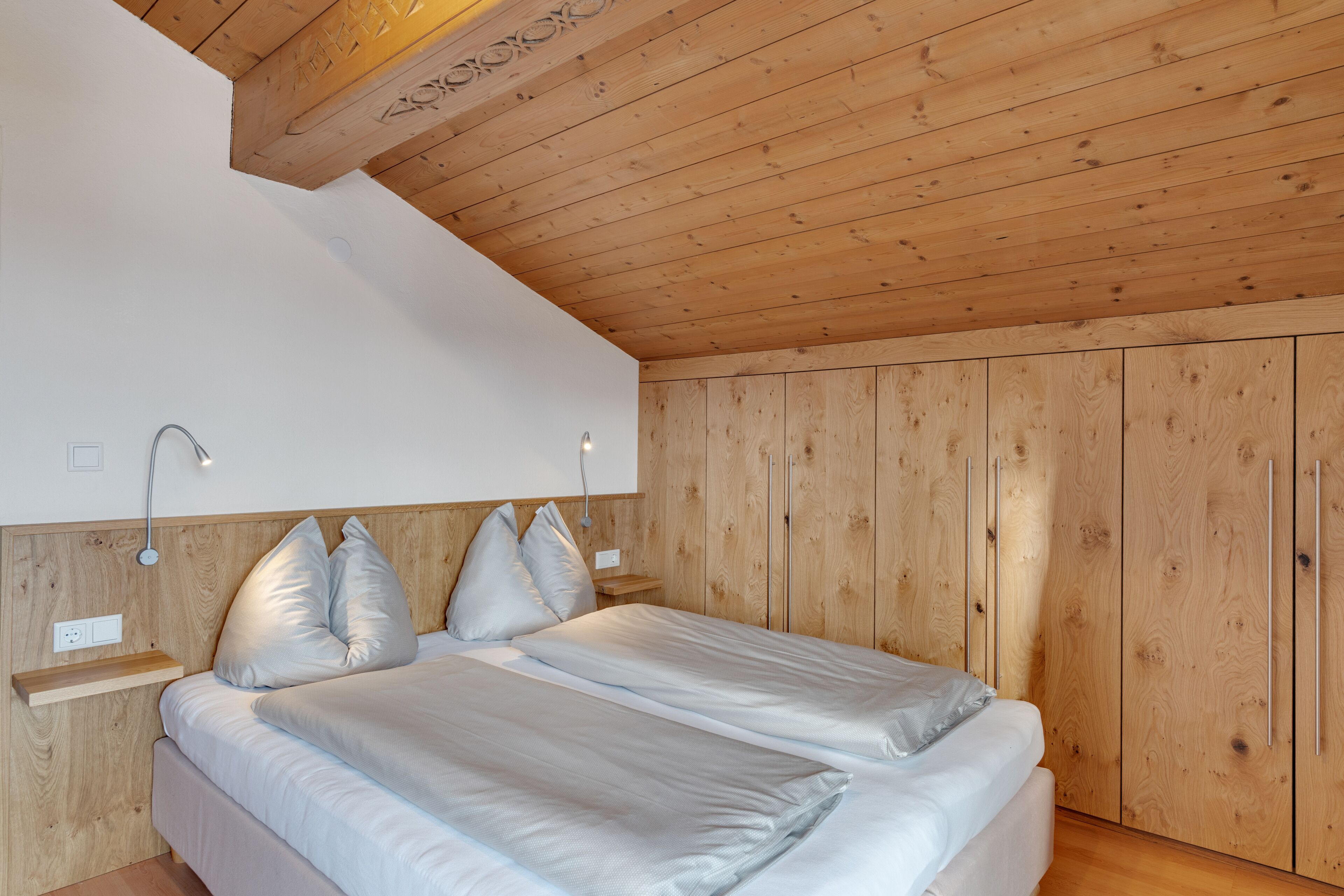 Un dormitorio con techo de madera, cama con ropa de cama blanca y paneles de madera en las paredes.