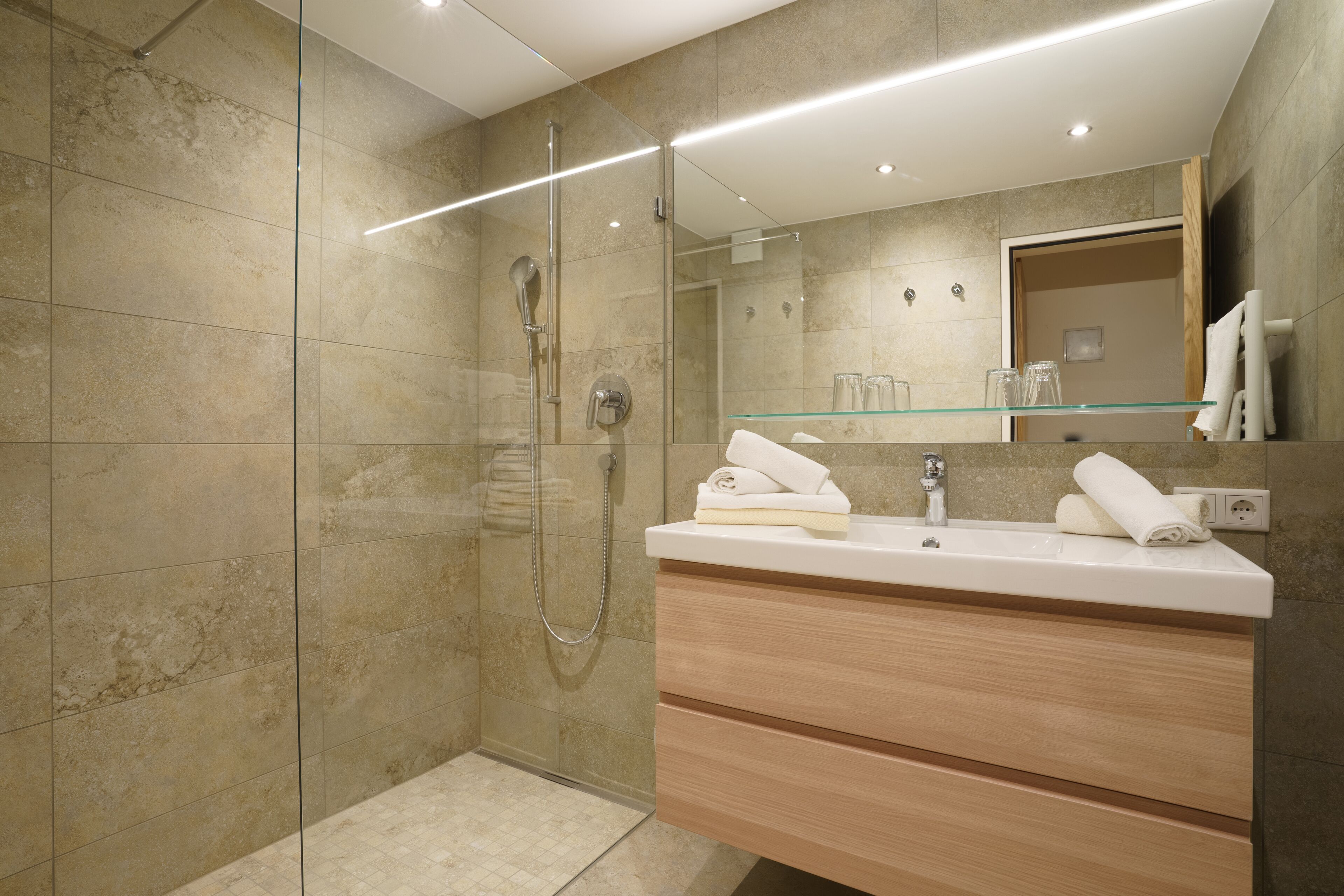 A modern bathroom with a glass-enclosed shower, a wooden vanity with a mirror, and a glass shelf.