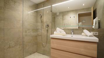 A modern bathroom with a glass-enclosed shower, a wooden vanity with a mirror, and a glass shelf.