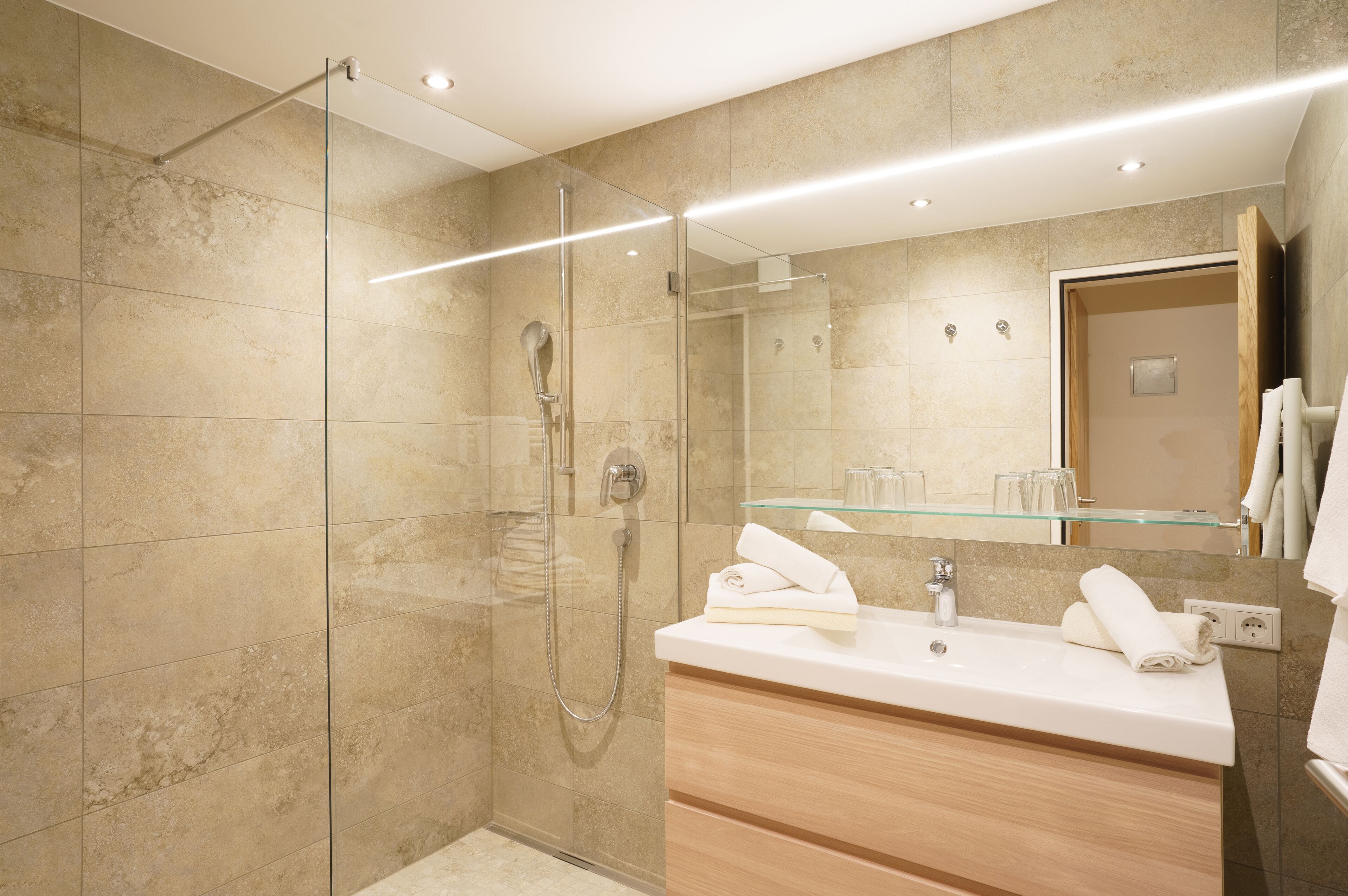 Une salle de bain moderne dotée d’une douche à parois de verre, d’un meuble-lavabo avec un miroir et d’une étagère en verre au-dessus du lavabo.