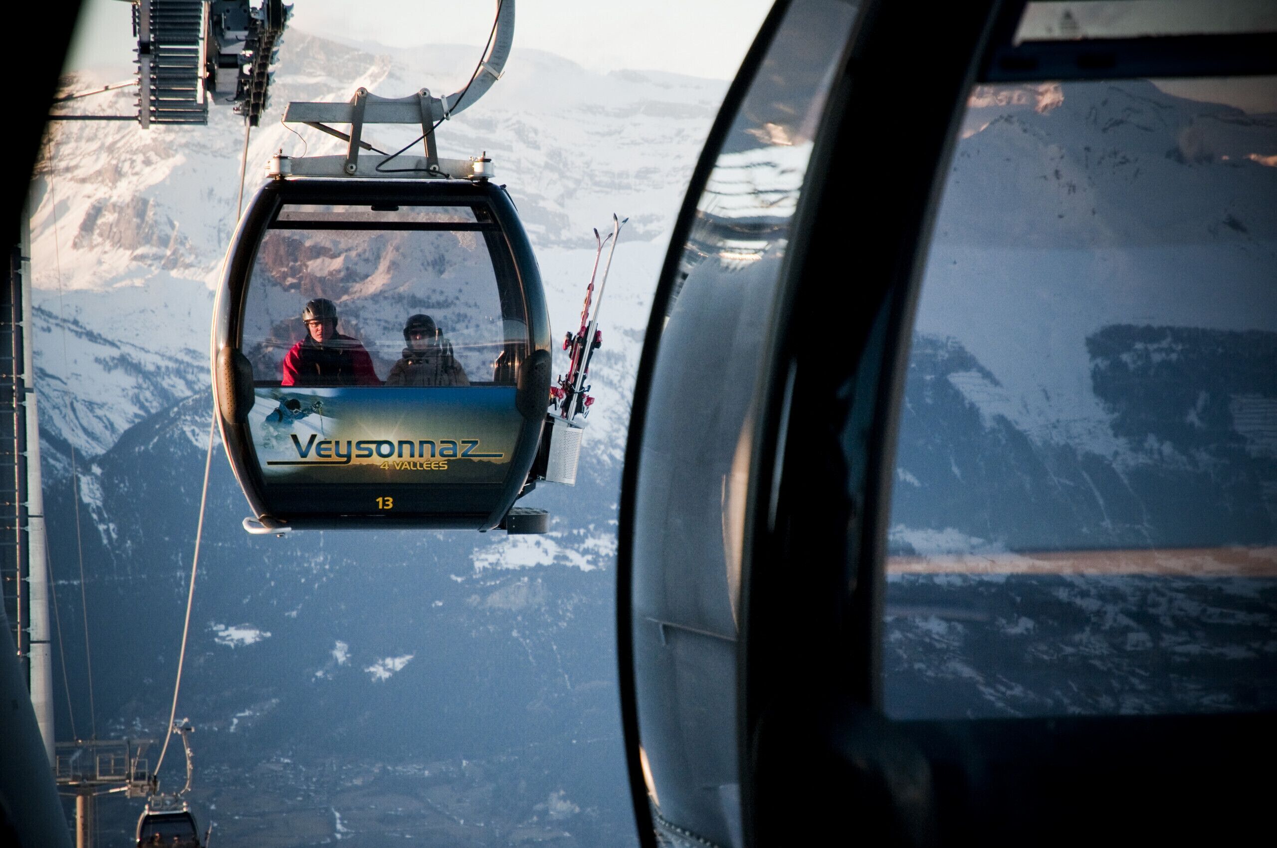 A cable car with passengers, labeled "Veisfonna 4 Vallees," moving over a mountainous landscape.