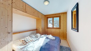 Ein kleines, gemütliches Schlafzimmer mit Etagenbett, Holzwänden, einem Fenster mit Blick auf Schnee und einem gerahmten Bild an der Wand.
