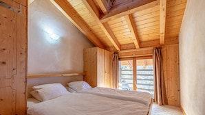 A wooden cabin bedroom with two beds, a sloped ceiling, and a window with curtains. - Balcons du Soleil Y2 221 - QUIET apartment 8 pers (Veysonnaz)
