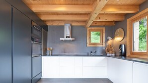 Cozinha moderna com armários cinza, eletrodomésticos de aço inoxidável, teto de madeira e janela com vista para o verde.