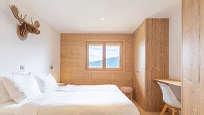 Quarto com parede de madeira, cama com roupa de cama branca, escrivaninha de madeira e uma cadeira.