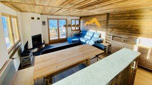 A wooden interior with a large wooden table, a blue sofa, and a television. - Fontanettaz V 007 - MOUNTAIN apartment 8 pers (Veysonnaz)