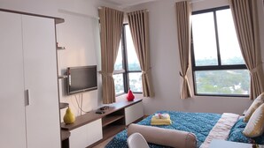 A hotel room with a bed, a TV, a desk, and a window with curtains.