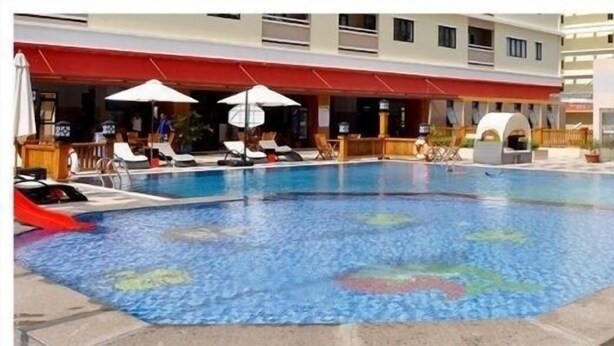 A swimming pool with lounge chairs and umbrellas, a covered seating area, and a building with signage.