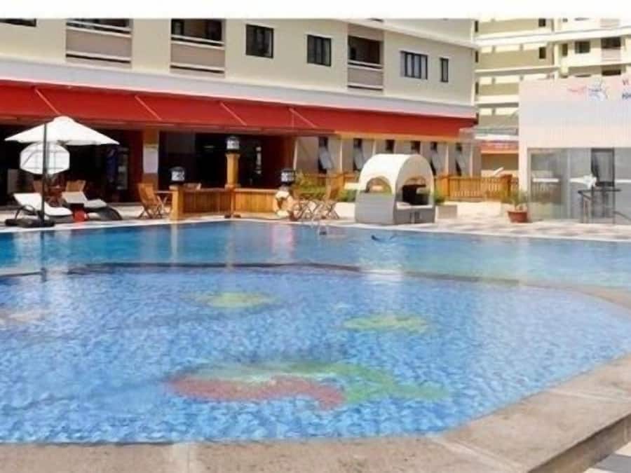 A swimming pool with lounge chairs and umbrellas, a covered seating area, and a building with signage.