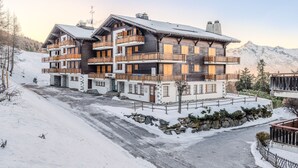 A multi-story hotel with wooden balconies and a ski slope in the background.