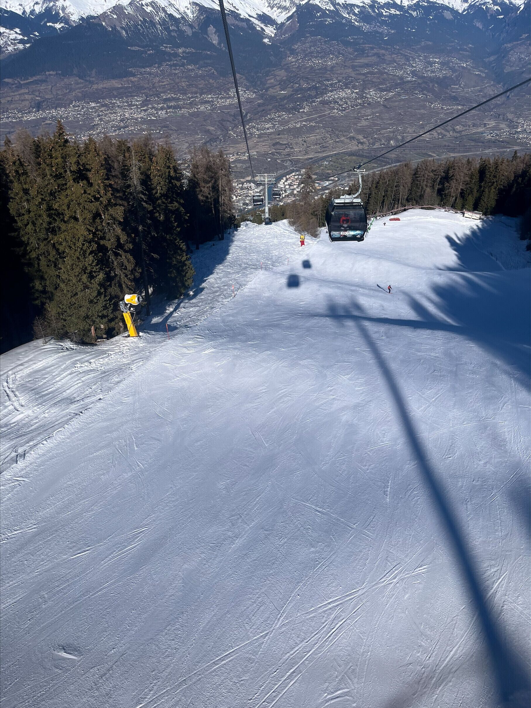 A ski lift chair moving along a snowy slope with a town in the background.