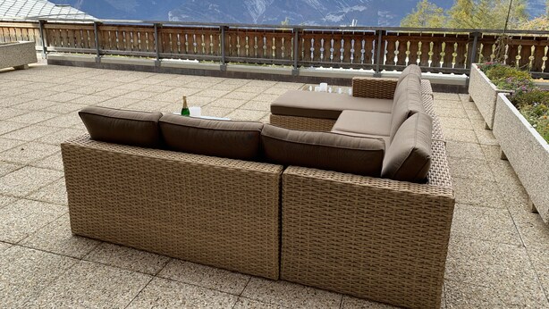 A wicker sofa set on a patio with a view of mountains.