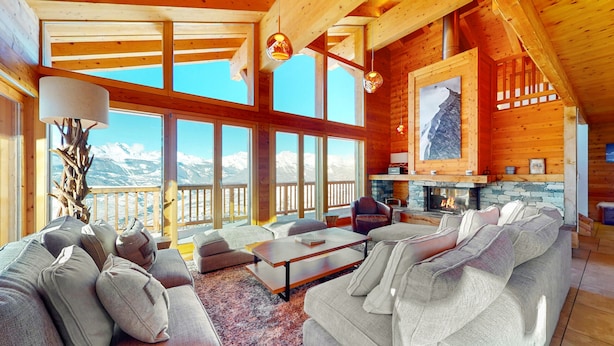 Un salón amplio con chimenea, ventanas grandes y vistas a montañas nevadas.