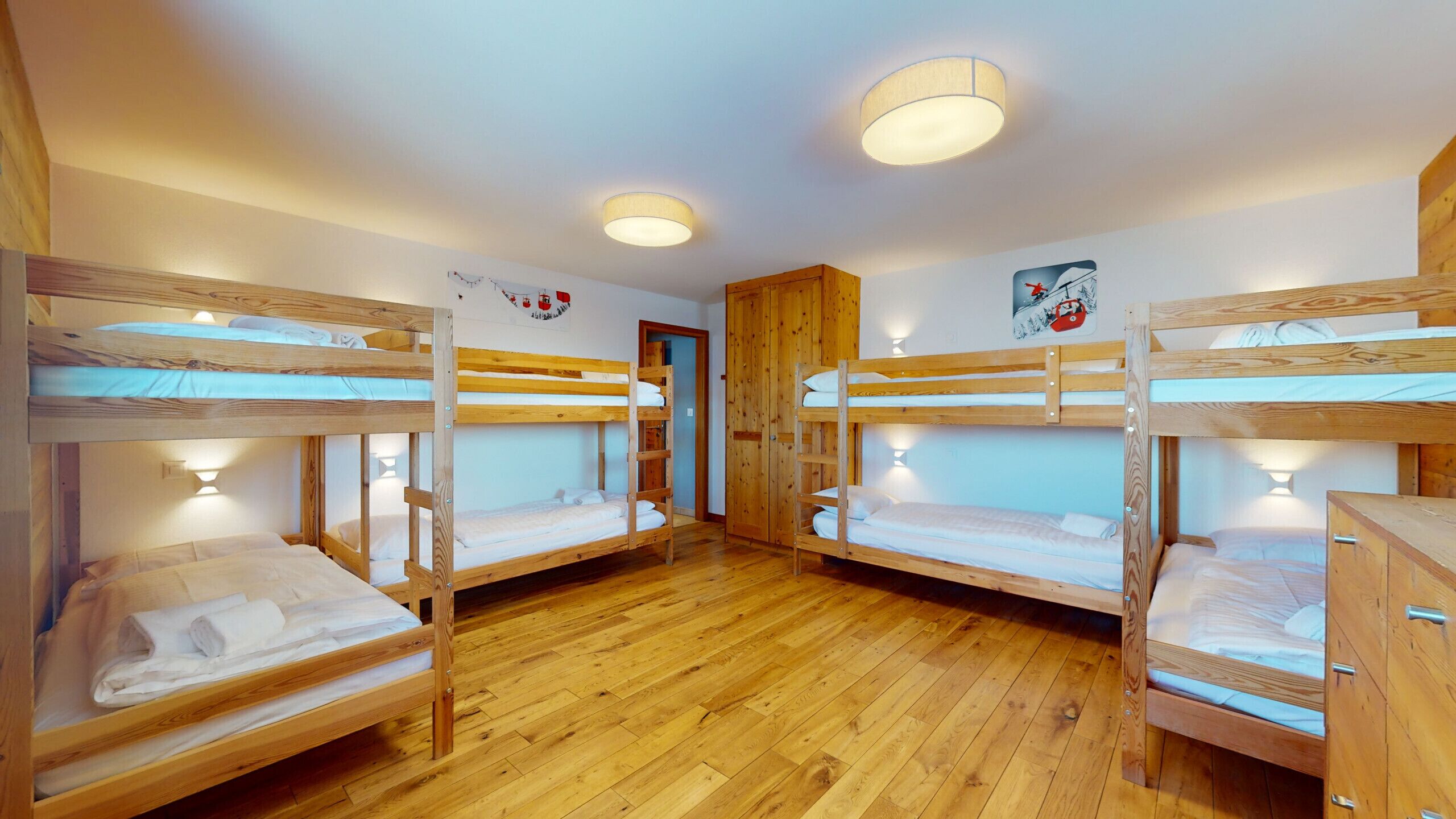 A room with four bunk beds, wooden flooring, and a wooden wardrobe.