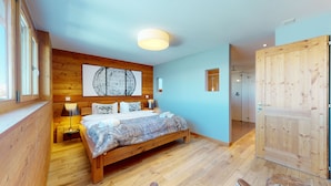 Un dormitorio con cama de madera, un ventanal grande, una puerta de madera y una lámpara en el techo.
