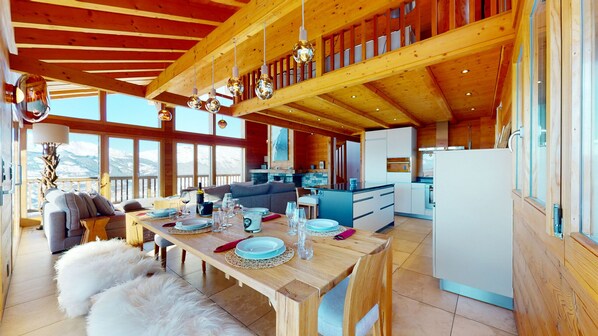 A spacious wooden cabin with a dining area, kitchen, and seating by a large window overlooking mountains. - Egg SAUNA & LUXURY chalet 16 pers (Veysonnaz)
