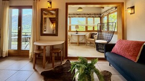 Une pièce chaleureuse avec des poutres apparentes, un coin repas, un canapé et une vue sur un balcon.