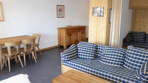 Un salon avec un canapé à carreaux, une table à manger en bois avec des chaises, un buffet en bois et un petit tableau encadré accroché au mur.