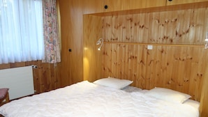 A wooden-paneled room with a bed, a nightstand, and a window with curtains.