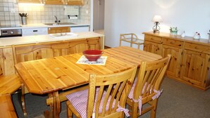 A wooden dining table with chairs, a red bowl, and a kitchen area with wooden cabinets and a sink.