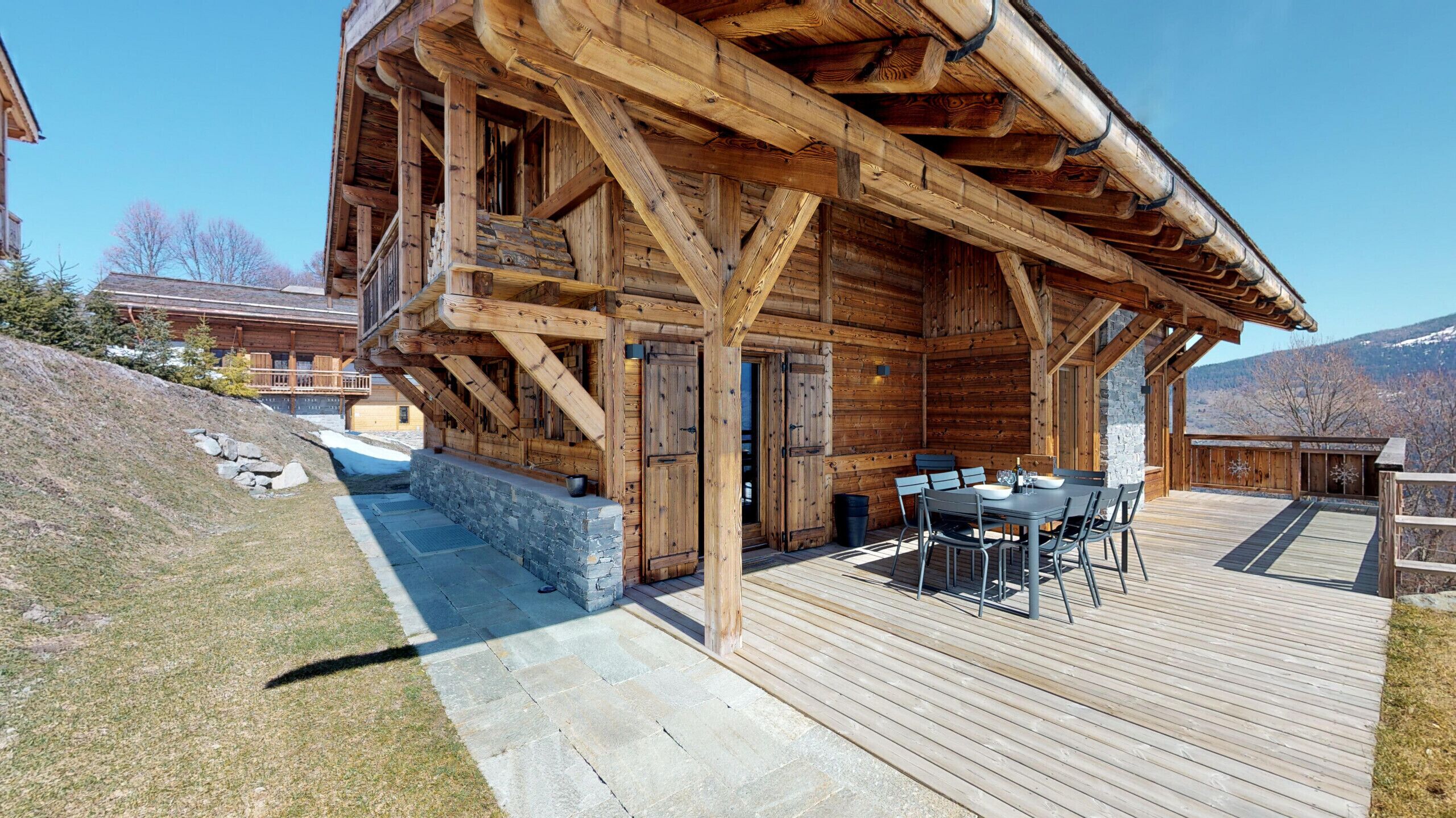 A wooden cabin with a deck, stone steps, and a table with chairs.