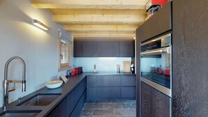 Een moderne keuken met een groot eiland, roestvrijstalen apparatuur en een houten plafond.