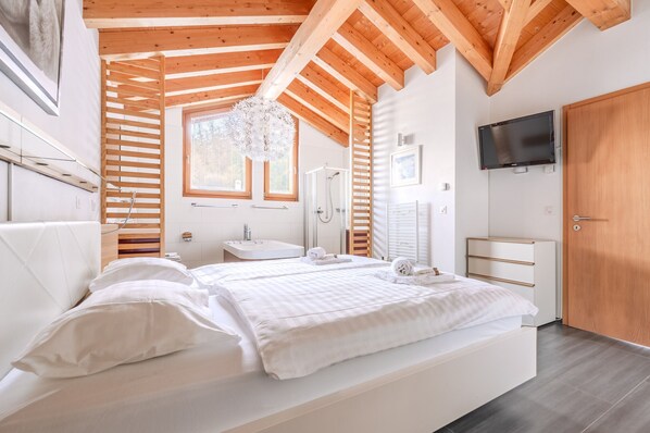 Un dormitorio moderno con techo de madera, una cama grande, una mesita de noche, un televisor y un baño con ducha.