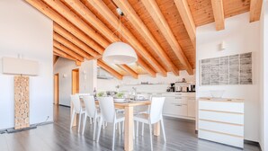 A modern kitchen with wooden beams, a dining area with white chairs, and a large window.