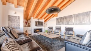 A modern living room with a fireplace, leather sofas, and a wooden ceiling.