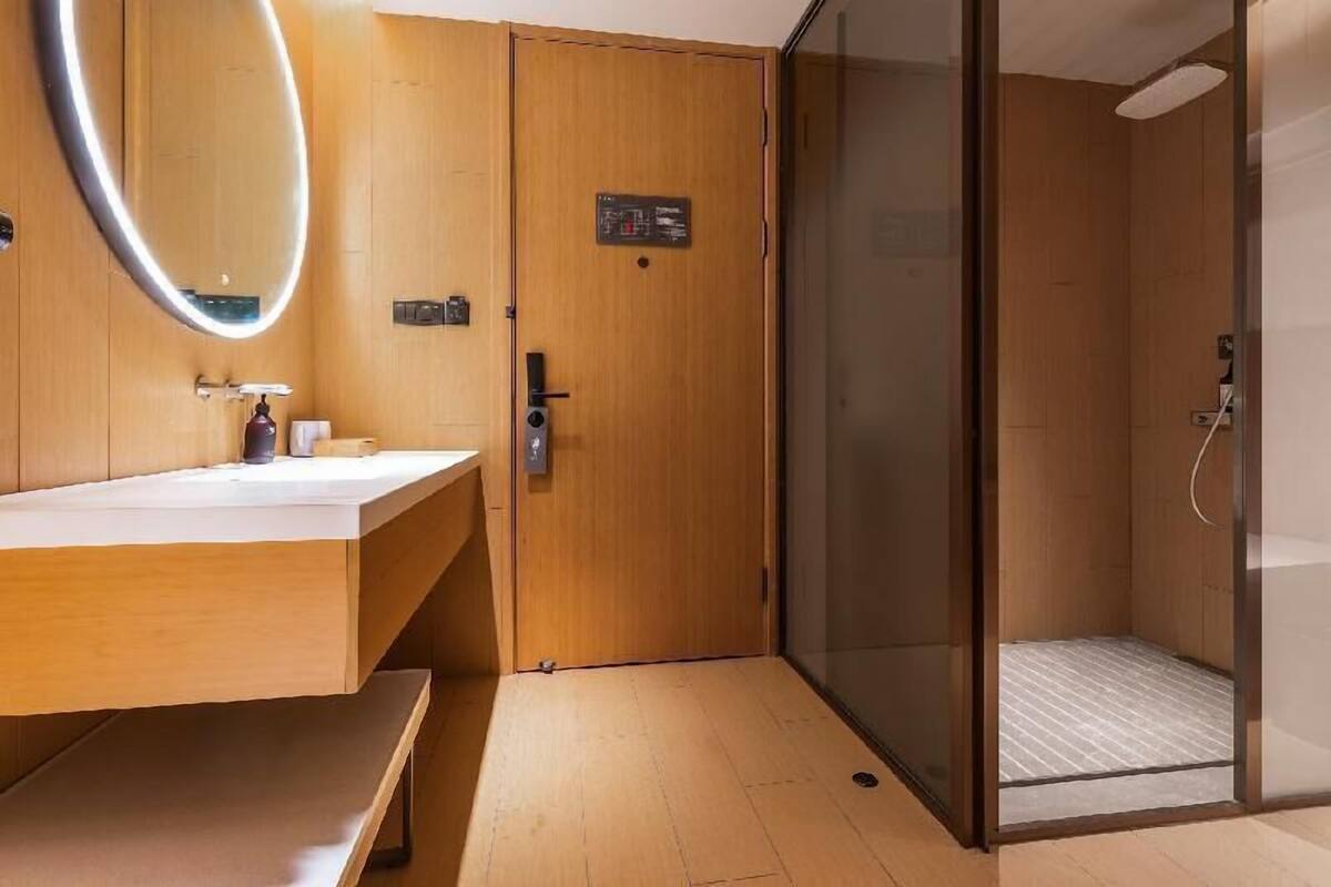 A modern bathroom with a wooden vanity, a glass shower enclosure, and a visible control panel.