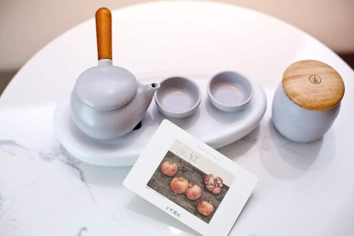 A white marble table with a teapot, two teacups, a small teapot, and a card with fruit illustrations.