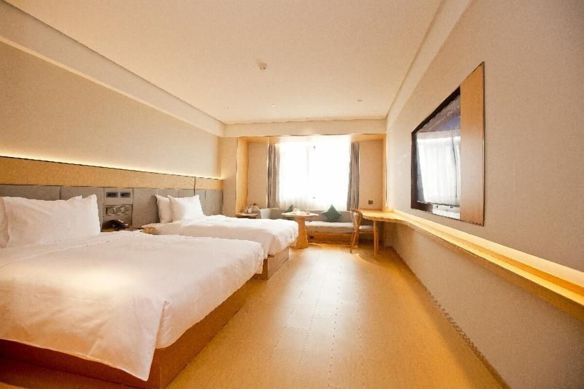 A hotel room with two beds, a desk, a chair, and a large window.