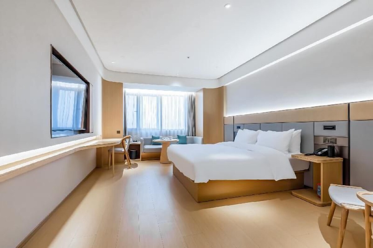 A modern hotel room with a large bed, a desk, a chair, and a small table.